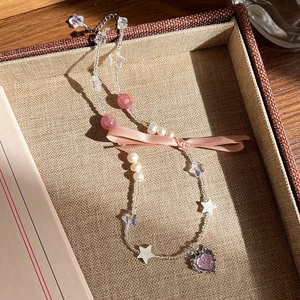 Détail du collier de perles avec pendentif cœur rose et nœud satin sur plateau tressé