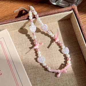Détails de nœuds en ruban rose et de pendentifs cœur irisés sur un collier de perles