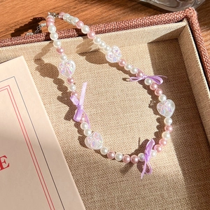 Détail du collier de perles avec perles roses, breloques cœur et un nœud en ruban violet