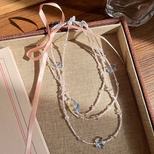 Détail d'un collier de perles multicouches avec nœud en satin rose et papillons nacrés