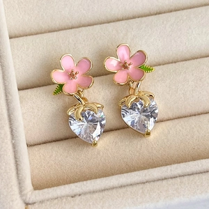 Close-up of pink flower enamel earrings with heart-shaped crystal pendants on velvet