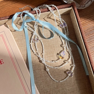 Détail d'un collier de perles avec rubans bleus et papillons sur un plateau en tissu