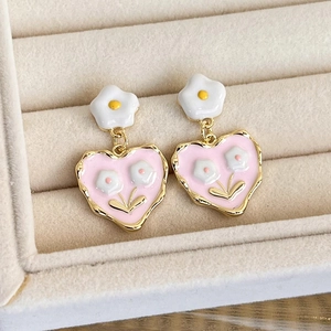 Detailed close-up of sweet pink heart earrings with white flower enamel and gold trim