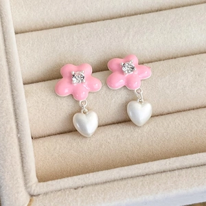 Close-up of pink flower earrings with heart charms and sparkling zircon centers