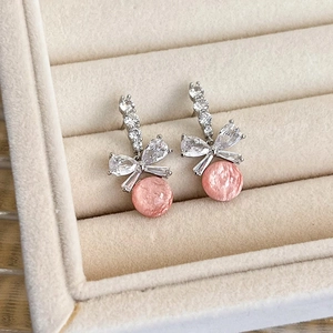 Detail of pink crystal drop earrings with crystal-studded bows on beige velvet base