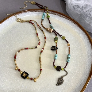 Vintage bohemian beaded necklace with green leaf pendant and colorful beads in a ceramic tray