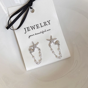 Détail de boucles d'oreilles étoile de mer et perles avec diamants sur carte bijou