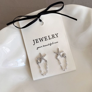 Détail de boucles d'oreilles étoile de mer argentées avec pompons de perles blanches