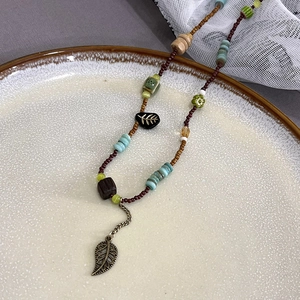 Detail view of ethnic beaded necklace with green leaf pendant on a beige ceramic plate