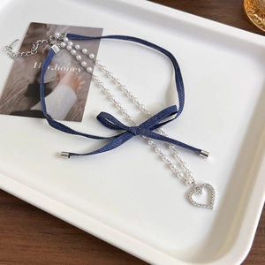 Detail of denim bow choker with pearl chain and heart pendant on a white tray