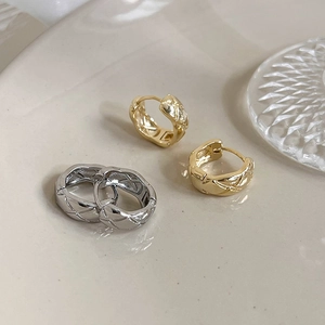 Macro shot of gold and silver quilted lattice wide hoop earrings on ceramic