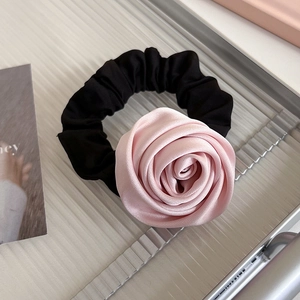 Gros plan du chouchou rose en satin avec pétales superposés et élastique noir