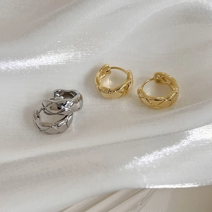 Macro detail of quilted pattern on gold and silver hoop earrings with a polished finish