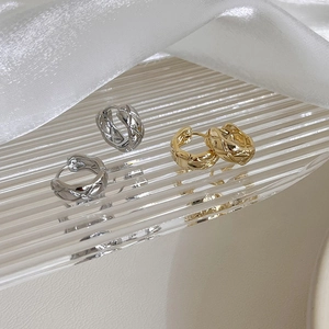 Close-up of gold and silver quilted metal hoop earrings on textured glass