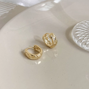 Close-up of golden quilted texture hoop earrings on a decorative ceramic tray