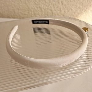 Detail of white jacquard satin headband with handmade label on decorative glass tray
