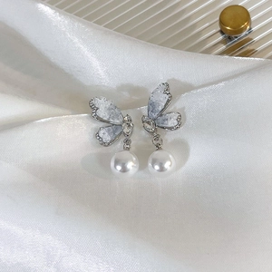 Elegante Kristall-Schmetterlingsohrringe mit weißen Perlen auf weißem Satin-Hintergrund