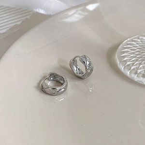 Close-up of silver metal hoop earrings with quilted pattern on a ceramic tray