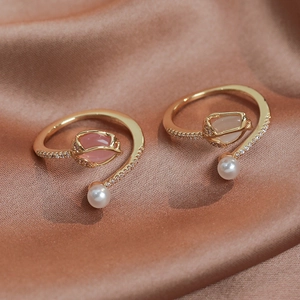 Detailed view of tulip rings with pink and white gemstones and pearls on satin fabric