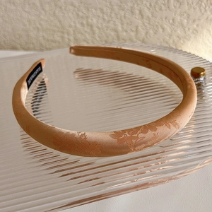 Detailed macro view of champagne satin headband with elegant leaf jacquard pattern texture