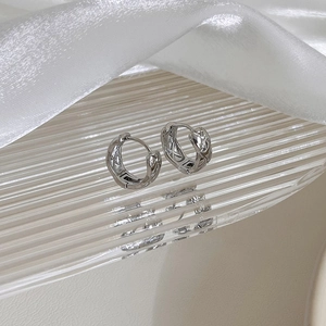 Macro shot of silver quilted pattern hoop earrings on a textured glass tray