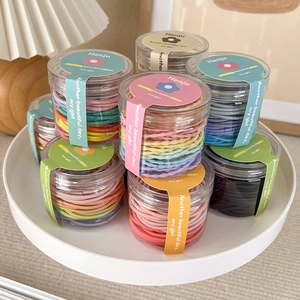 Detail view of colorful elastic hair ties in a clear cylinder jar on a white tray