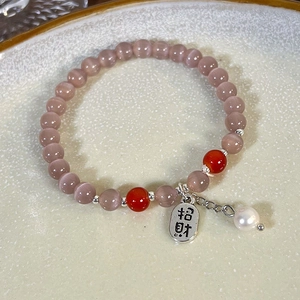 Nahaufnahme von Katzenaugen-Perlenarmband mit silbernem Glücksanhänger auf Tablett