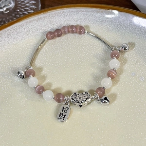 Makroaufnahme von Katzenaugen-Perlenarmband mit Glücksbringer und Glocke auf Keramik