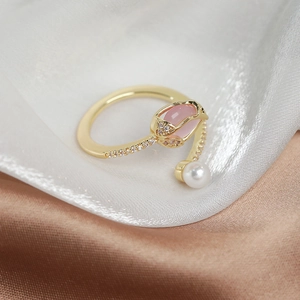 Detailed macro view of gold tulip ring with pink crystals and a white pearl on silk