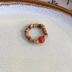 Detail view of handmade beaded ring with brown wooden beads and a red agate stone accent