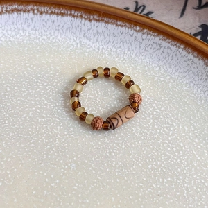 Detail of handmade vintage beaded ring with amber beads and wood cylinder on ceramic plate