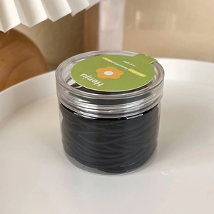 Detail of high-elasticity black hair ties set in a clear cylindrical jar with green label
