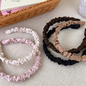Close-up of pleated satin headbands in earth tones displayed on a white textured background