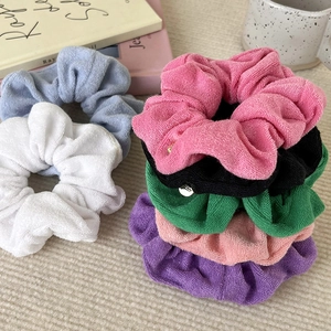 Close-up of colorful terry cloth hair scrunchies with small metal logo tags on fabric