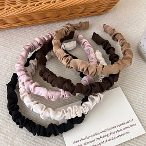 Detail view of five assorted satin pleated headbands in earthy tones arranged on a textured surface