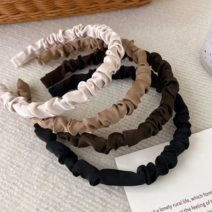 Pleated satin headbands set in earth tones displayed on a textured fabric background