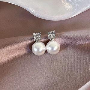 Elegant square pave diamond stud earrings with white pearl pendants on satin background