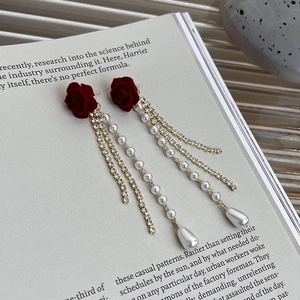 Détail de boucles d'oreilles camélia en velours rouge avec de longs pompons perles