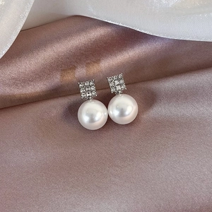 Close-up of pearl stud earrings with square diamond settings on elegant champagne silk