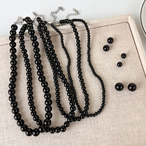Detail of black glass beaded necklaces and stud earrings on a beige woven tray