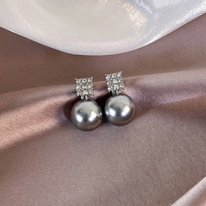 Detailed close-up of French style earrings with cubic zirconia and gray pearl on silk cloth
