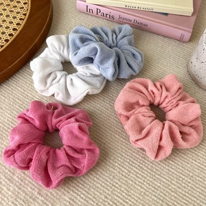 Detail of four colorful towel fabric scrunchies with small gold pendants in a soft setting
