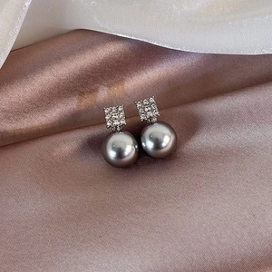 Detailed view of grey pearl earrings with square rhinestone accents on silk background