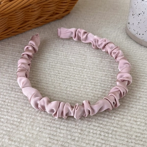 Close-up of pink pleated satin headband with elegant scrunchie texture and soft fabric