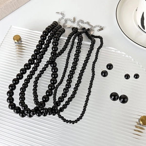 Black glass bead necklace and earring set on a textured glass tray in a bright setting