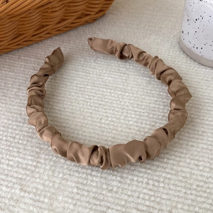Detail of earthy tone pleated satin headband featuring elegant silk texture on neutral base