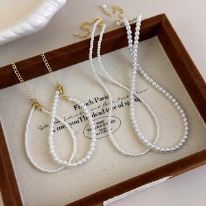Close-up of white faux pearl necklace set with golden lobster clasps on a wooden tray