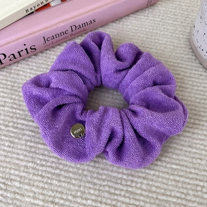Detail of purple terry cloth scrunchie with round silver metallic logo tag on a white fabric