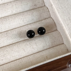 Detail view of round black bead stud earrings on beige linen jewelry box texture