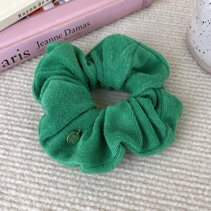 Detail of green towel fabric scrunchie with round metal charm on textured background